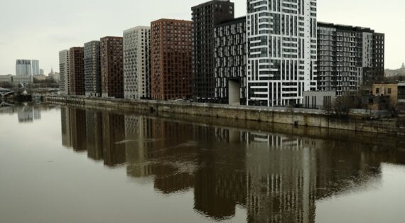 Captivating view of modern high-rise buildings reflecting in a calm river under cloudy skies.