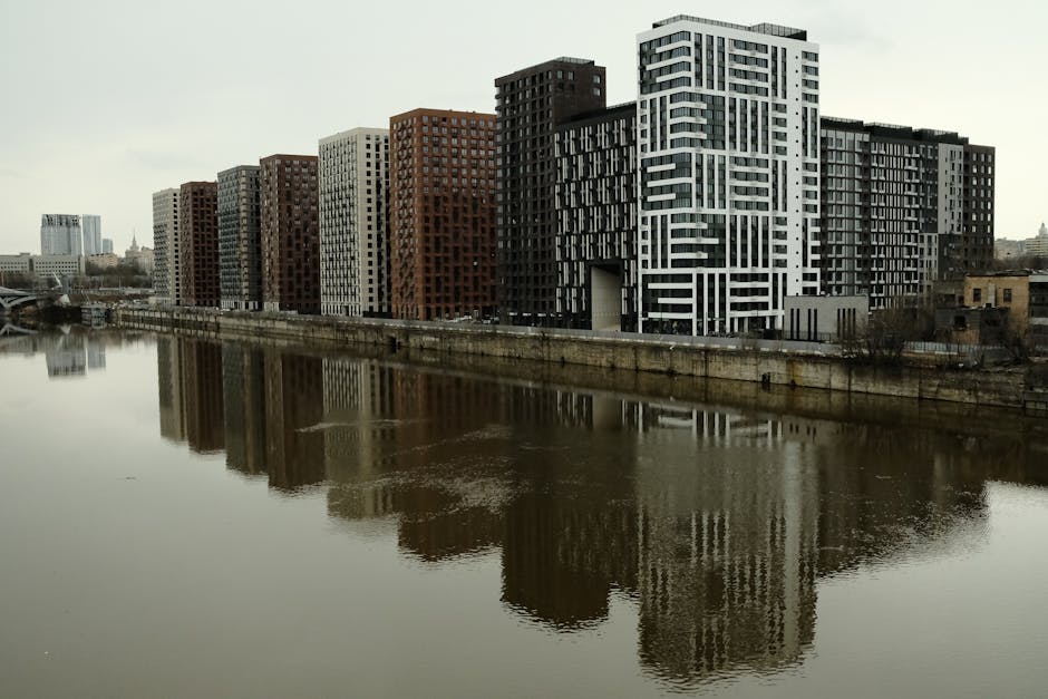 Captivating view of modern high-rise buildings reflecting in a calm river under cloudy skies.