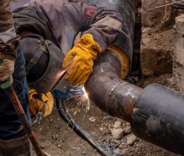 Close-up of a skilled worker welding a steel pipe outdoors at a construction site.