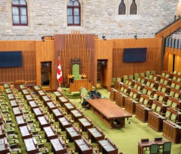 Interior view of the Canadian House of Commons with green seating and wooden decor.