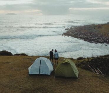 Two tents and a couple enjoying a scenic coastal view in Palhoça, Brazil.