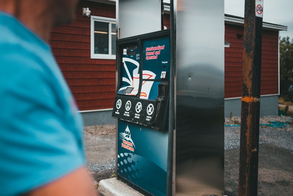A close-up of a gas pump with a person nearby in Newfoundland, outdoors.