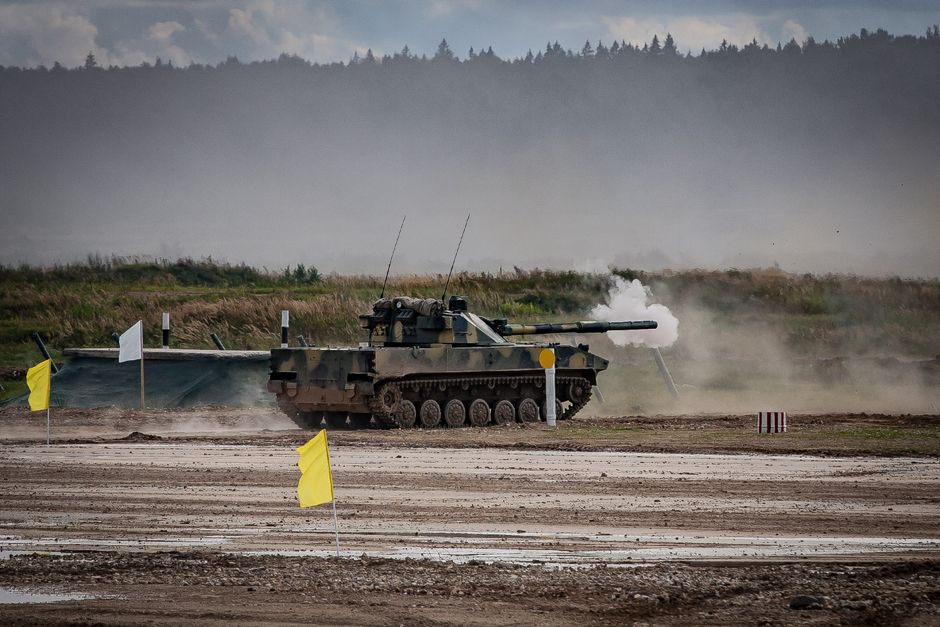 A military tank firing a shell during training in an open field.