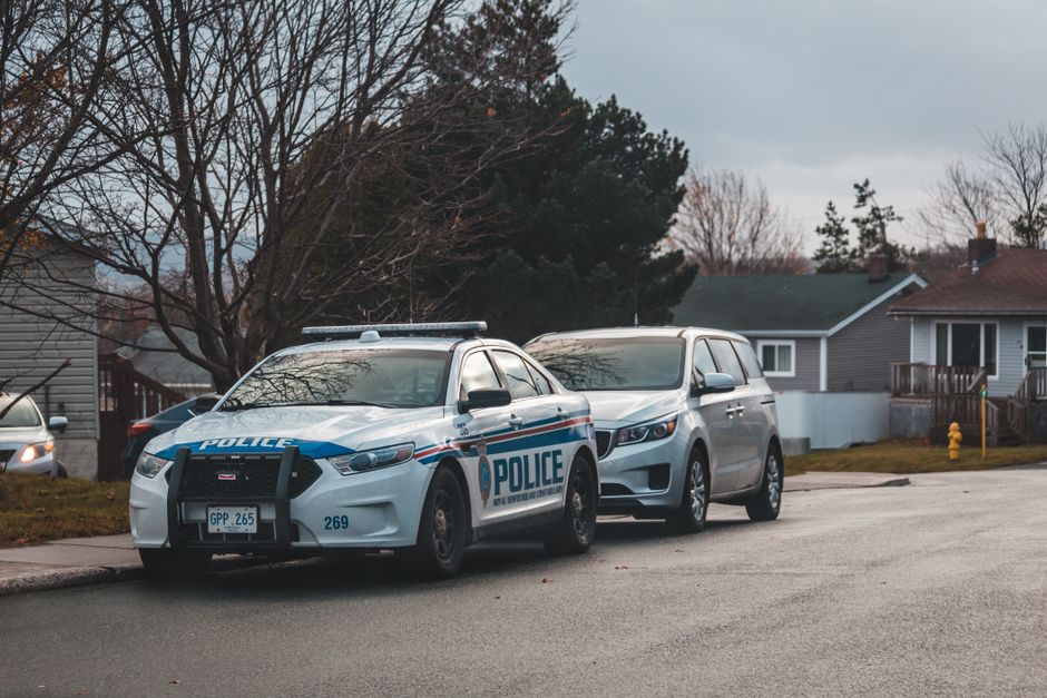 A suburban street with a police car and parked vehicles. Captured in daylight.