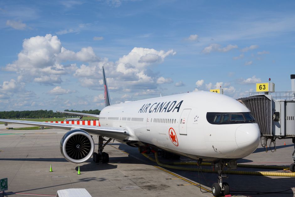 Air Canada Boeing 777 airplane parked at an airport gate under a clear blue sky.