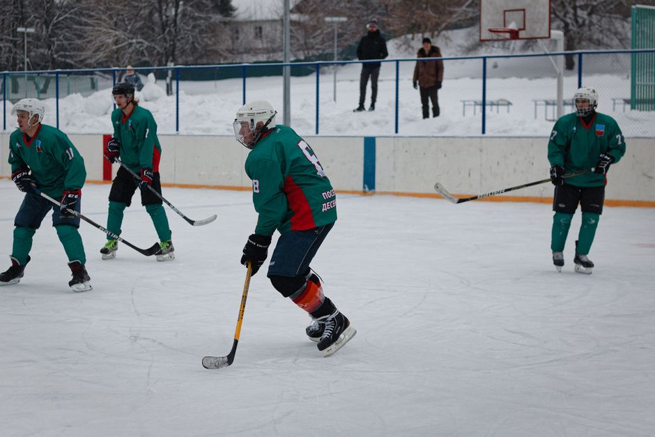 Amateur ice hockey match in snow-filled setting with players in green uniforms.