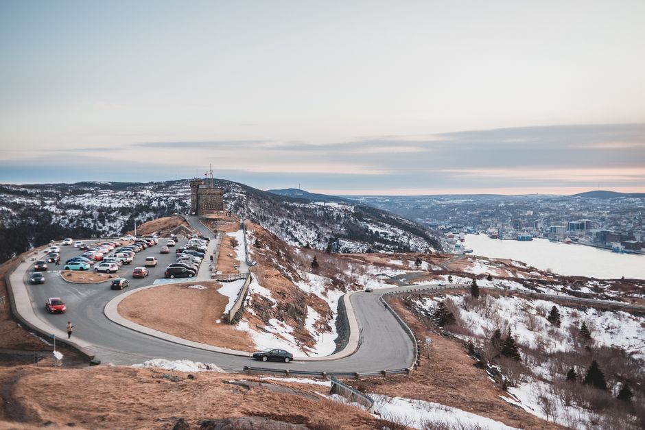 Automobiles riding on curvy asphalt roadway near grassy shore covered with snow against river and cloudy sky on winter day