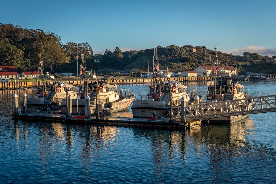 Coast Guard boats docked at a peaceful harbor under a clear blue sky, reflecting the crisp morning light.